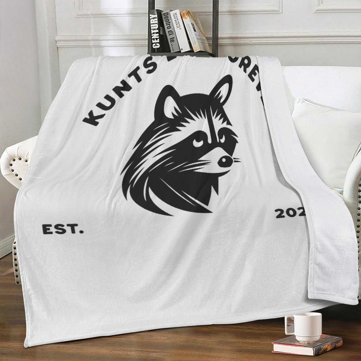 White soft cotton blanket with black rebellious raccoon graphic and text "KUNTS" and "EST. 2023", styled in punk streetwear design